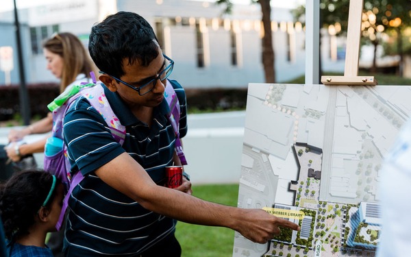 Person points to a site plan map on an easel while standing with a child at an outdoor event.