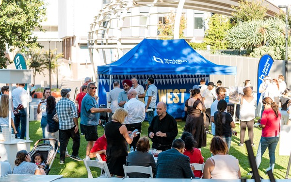 Community members gather on a lawn around a blue Blacktown Quarter event tent during an outdoor kickoff event.