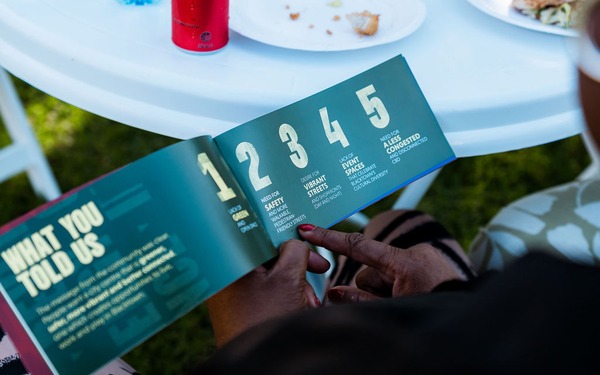 Close-up of hands holding an open brochure showing community feedback priorities and numbered points.