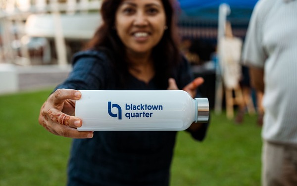 Person holds a white Blacktown Quarter branded drink bottle toward the camera.